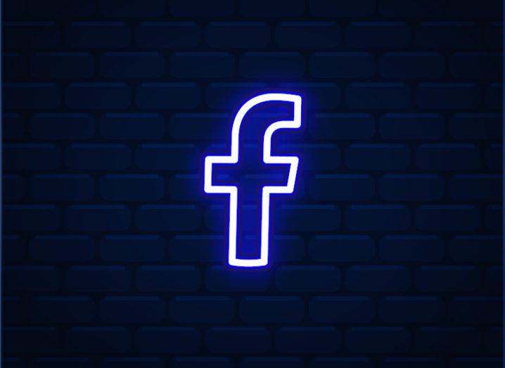 A neon Facebook logo lights up against a darkened brick wall.