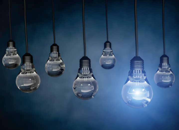 Seven lightbulbs hanging against a dark blue background. One of the bulbs is on with a bright blue light.