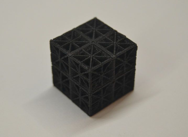 A black 3D-printed material in the shape of a cube with a lattice design on all sides.