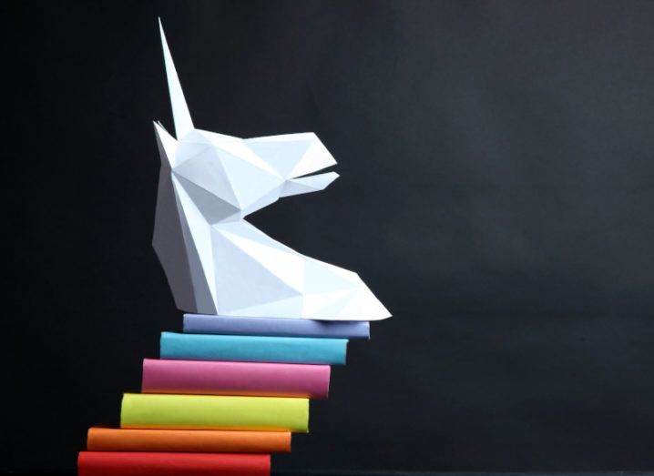 A white unicorn head statue balances on a colourful stack of blocks against a charcoal background.