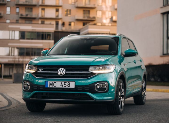 A green-blue Volkswagen T-Cross on a road with no one in the car.