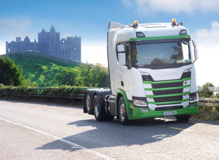 The front of a green and white truck parked on the side of a road with the Rock of Cashel in the background.