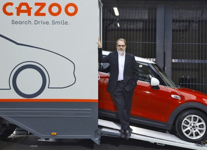The founder of Cazoo standing in front of a car. The car is coming out of a van that has the Cazoo logo on the side.