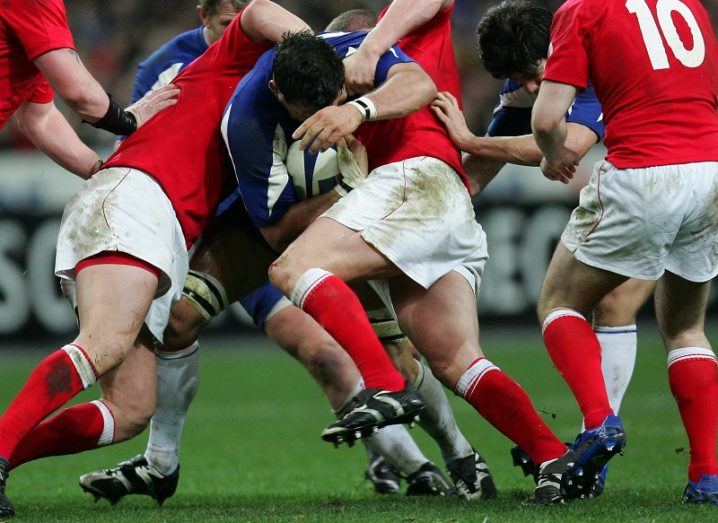 Rugby players tackling each for the ball on a sports pitch.