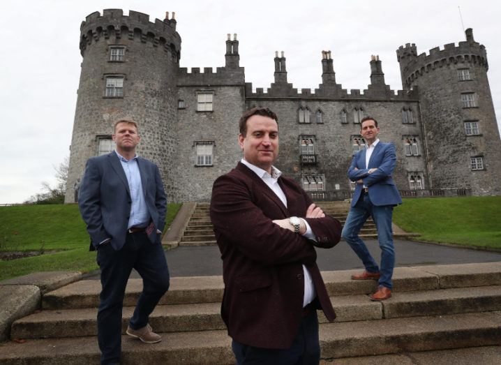 Three men are standing socially distanced outside a castle.