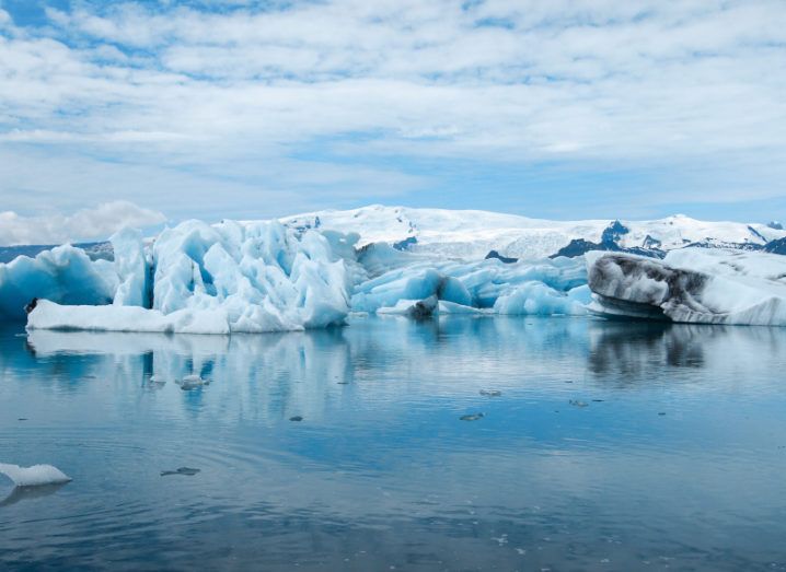 Glaciers melting in a blue ocean against a bright blue sky with clouds, showing the climate crisis.