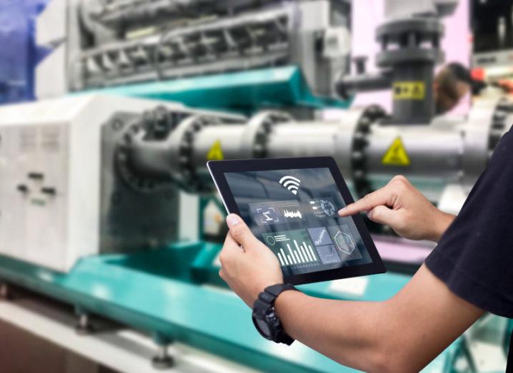 A man holding a tablet with a variety of graphs and data on it. There is machinery in the background, symbolising smart manufacturing.