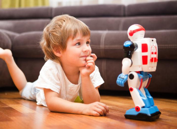 A little boy lying on a wooden floor, playing with robot toy.