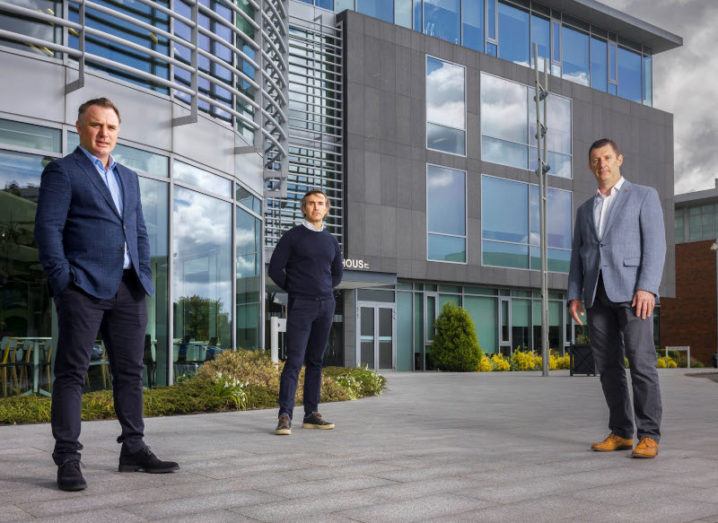 Three men stand socially distanced outside an office building.