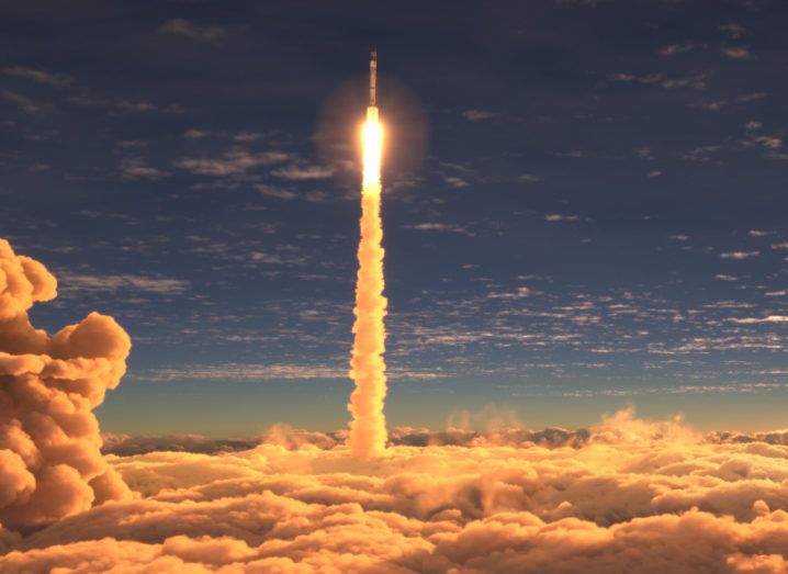 A rocket flies upwards through the sky at sunset. There’s a bed of clouds at the bottom of the picture.