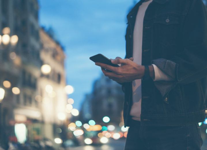 A man is using his smartphone on a city street at night.