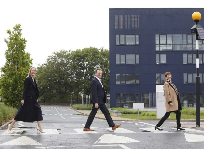 Three people walk across a zebra crossing in front of the large, blue IADT Media Cube building.