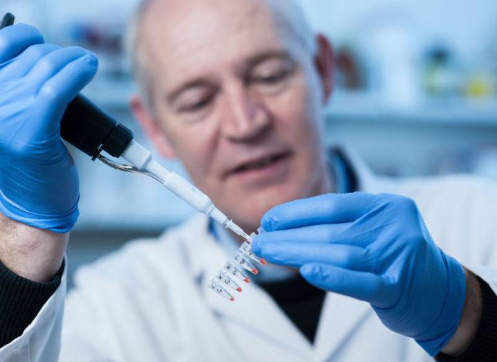 A man wearing protective gloves and a lab coat is filling vials in a lab setting.