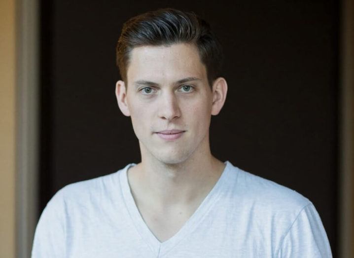 A young man with slicked-back hair wearing a white v-neck T-shirt.