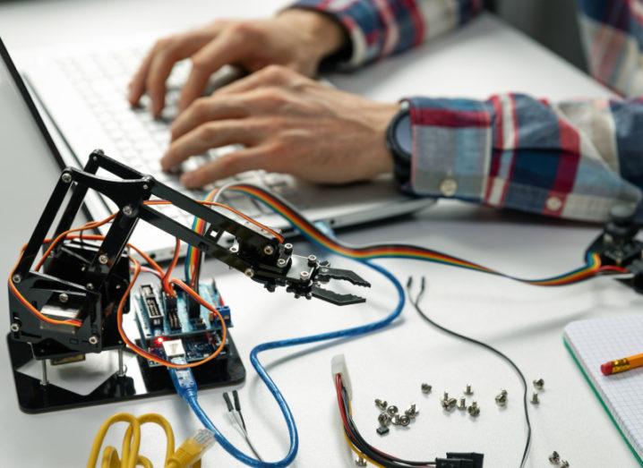 Shot of an engineer's hands working on a robotics project with various robotics and technical equipment laid out beside him on a desk beside a notebook and pencil.