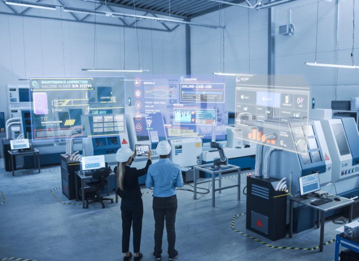 Two engineers stand on a factory floor wearing hard hats. Illustrations of digital interfaces emerge from the nearby equipment, demonstrating the digitisation of the manufacturing process.