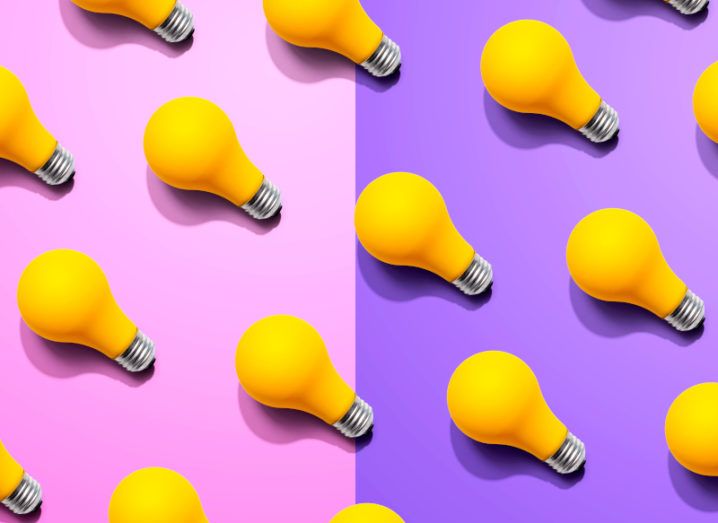 A number of yellow lightbulbs lined up in neat rows on a half pink, half purple background.