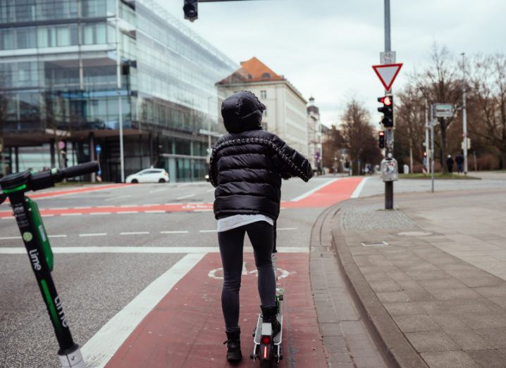 Woman rides an e-scooter on a city cycle lane surrounded by a city scape