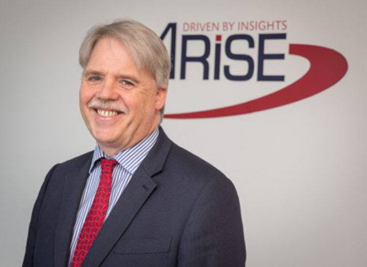 Joe Cahalane, managing director of Arise Europe, stands in front of the company's logo on a white background.