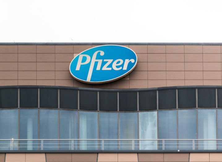 The Pfizer logo on the top of a brown office building against a bright white sky.