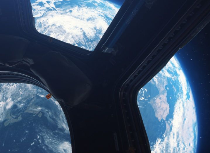 The Earth is pictured from inside the International Space Station. The curve of the Earth can be seen and glows brightly against the darkness of space.