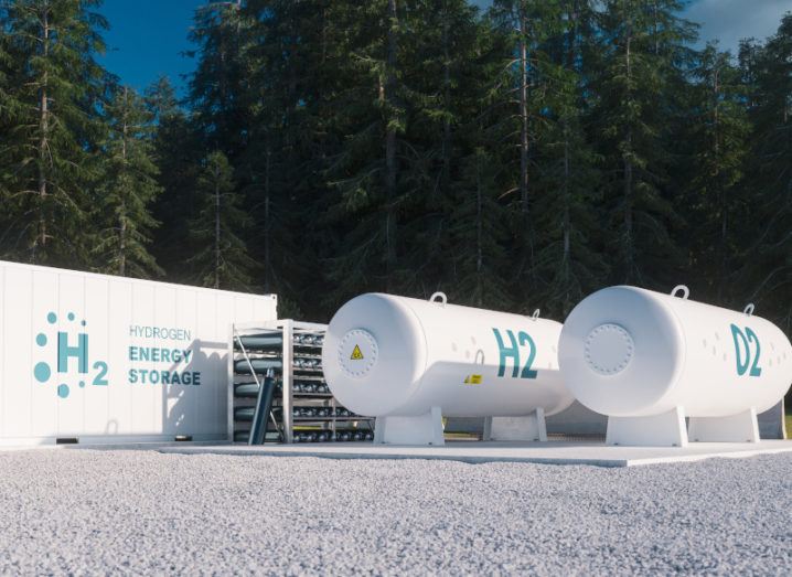 A hydrogen gas storage facility with two round tanks and one large rectangular storage box in front of forest.