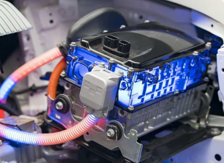 A battery used in electric vehicles is shown. There are two red tubes connected to the main body of the battery, which is black. The battery is also glowing blue.