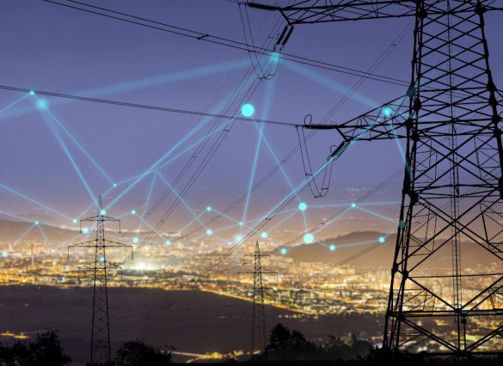 Image of electricity poles connected to each other with a city in the background.