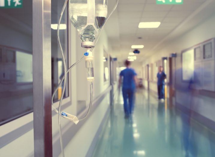 A hospital corridor is pictured where health projects are likely to be implemented. There is a drip directly in front of the camera and doctors and nurses can be seen in the background. It is a time lapse image and so the people are blurred to show that they are moving.