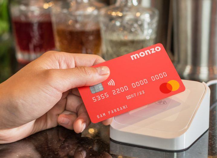 A hand holding a Monzo card and tapping it on a contactless payment machine.