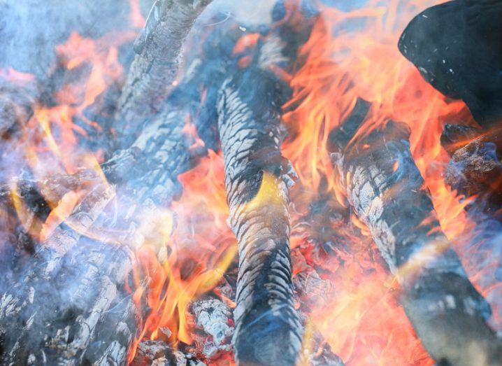 Wood is burning in a smoky fire with orange flames.