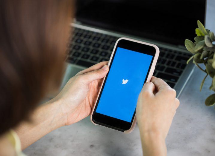 Woman holding a smartphone with Twitter logo on the screen.