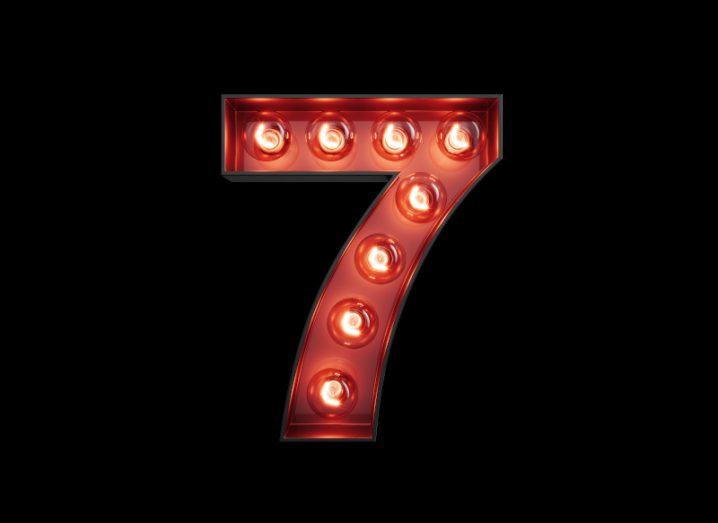 A large lightbox shaped like the number seven. Large round bulbs are set throughout, lighting up its red interior.