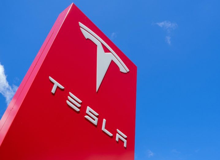 The Tesla logo at one of its dealerships under a bright blue sky.