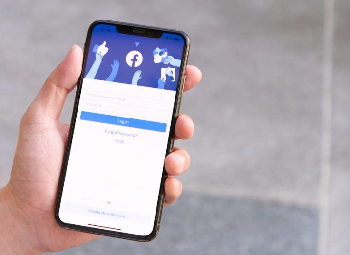 A person's hand holding a phone with the Facebook login page open on the screen.