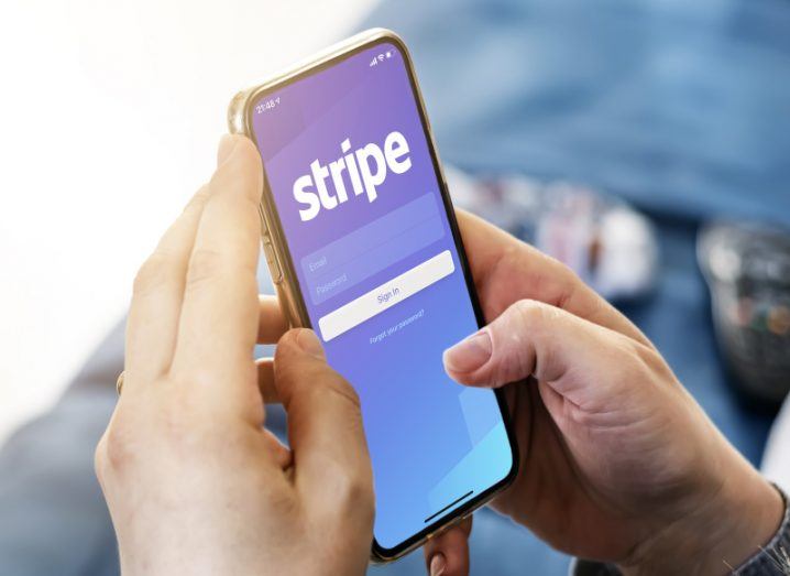 Pair of hands holding a smartphone with Stripe payment company logo displayed on the screen.