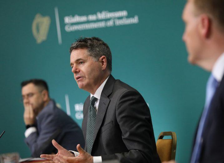 Minister Paschal Donohoe wearing a suit, sitting at a press conference table for Budget 2022.