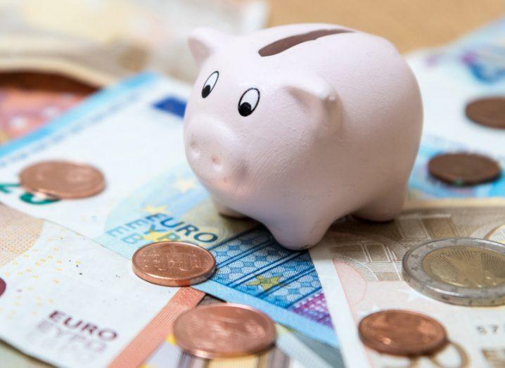 Pink piggy bank kept on top of euro notes and coins.