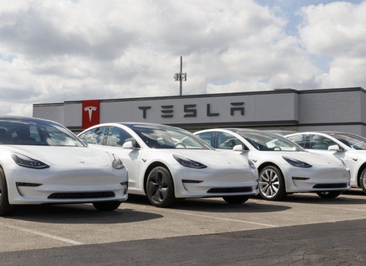 Four white Tesla electric cars in front of a Tesla building, with a cloudy sky hanging overhead.