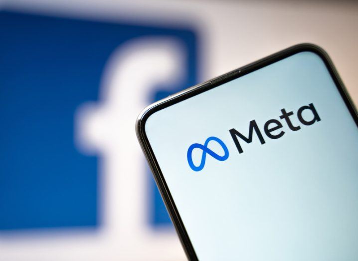 Smartphone screen with Meta logo on it. Facebook logo can be seen in the blurred background.