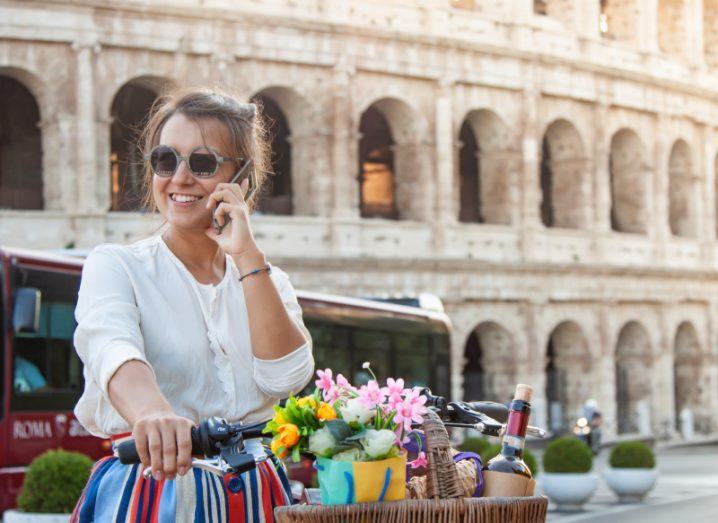 A woman speaks on her phone while passing the Colosseum in Rome on her bicycle.