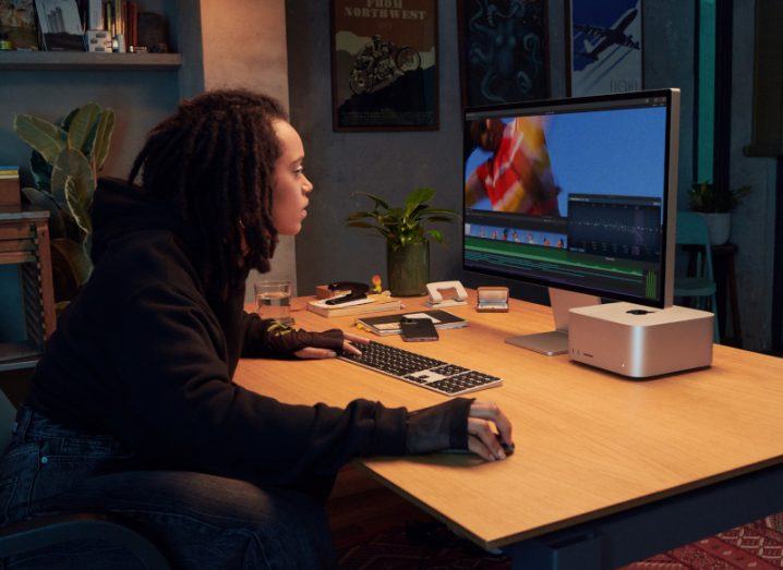 A person sitting in front of an Apple Mac display at a table.