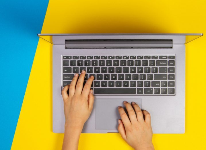 Person typing on a laptop against the blue and yellow colours of Ukraine.