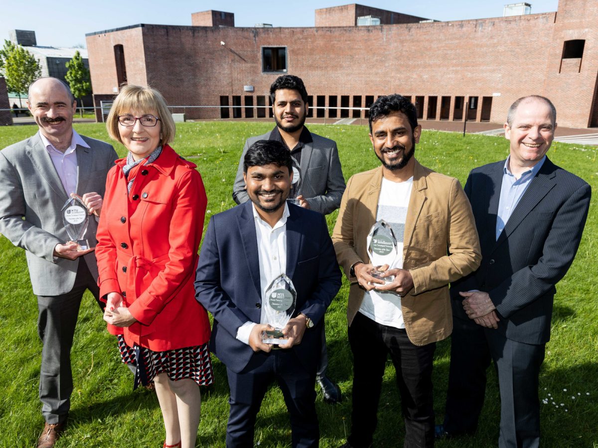 Five men and one woman standing on grass in front of a university building, with several of them holding awards. They are Dr William Whelan Curtain, Prof Maggie Cusack, Dr Chinna Devarapu, Adarsh Ananthachar, Dr Uday Gouda and Ronan Coleman.