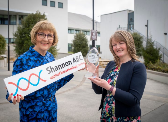 Photograph of two women standing next to each other. One is holding an award while the other has a sign that reads Shannon ABC, applied biotechnology centre.