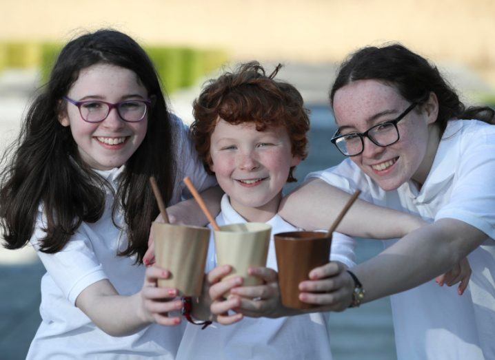 Two girls on either side of one boy, all holding biodegradable cups in their hands.