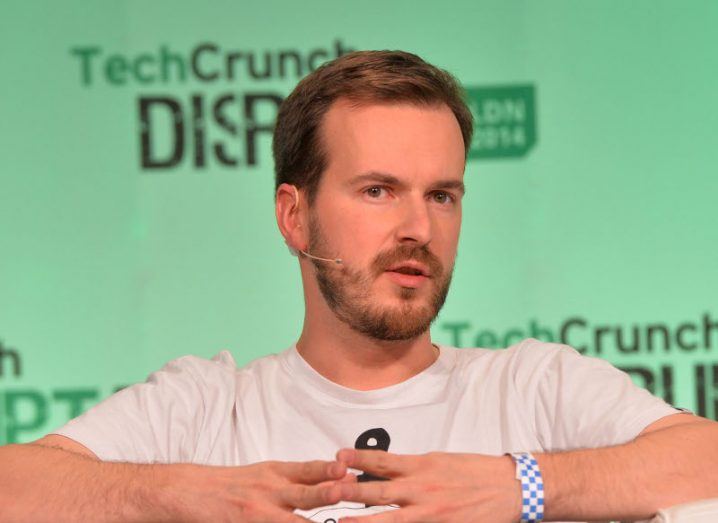 A man in a white T-shirt speaking at a TechCrunch event. He is Taavet Hinrikus, co-founder of Wise and a founding member of Plural.