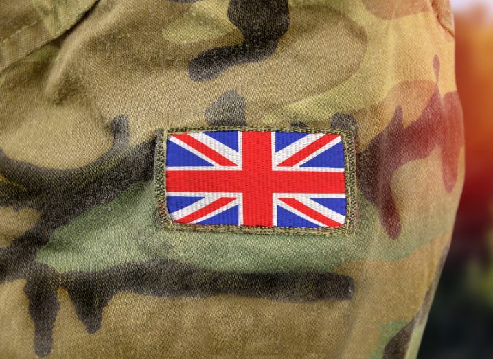 UK flag on the arm of a person wearing a camouflaged army uniform.