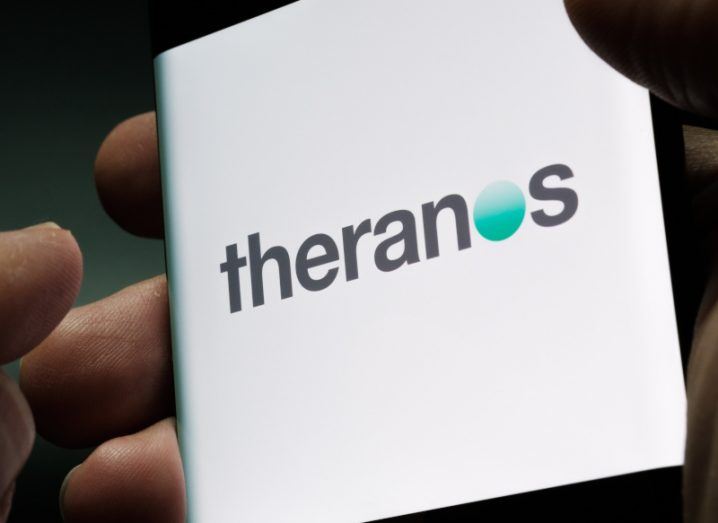 The Theranos logo shown on the screen of a smartphone held in a person's hands.