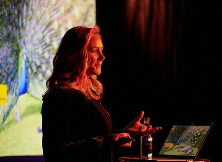 A woman standing on a stage, giving a talk at a podium.